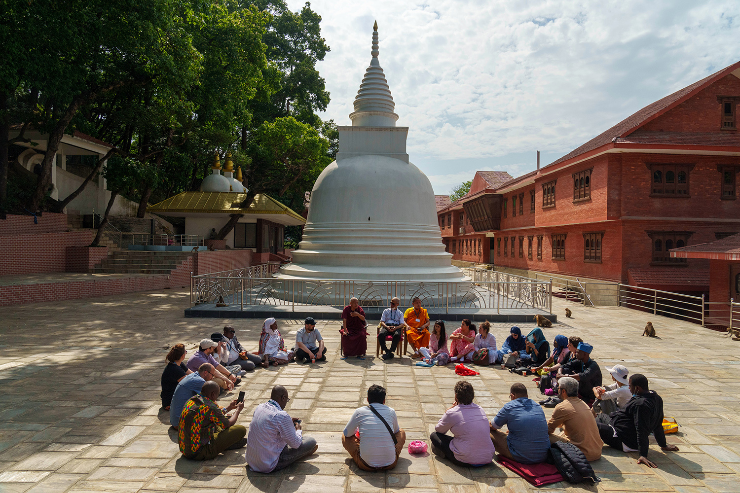 People sit in a circle before a white pagoda. 