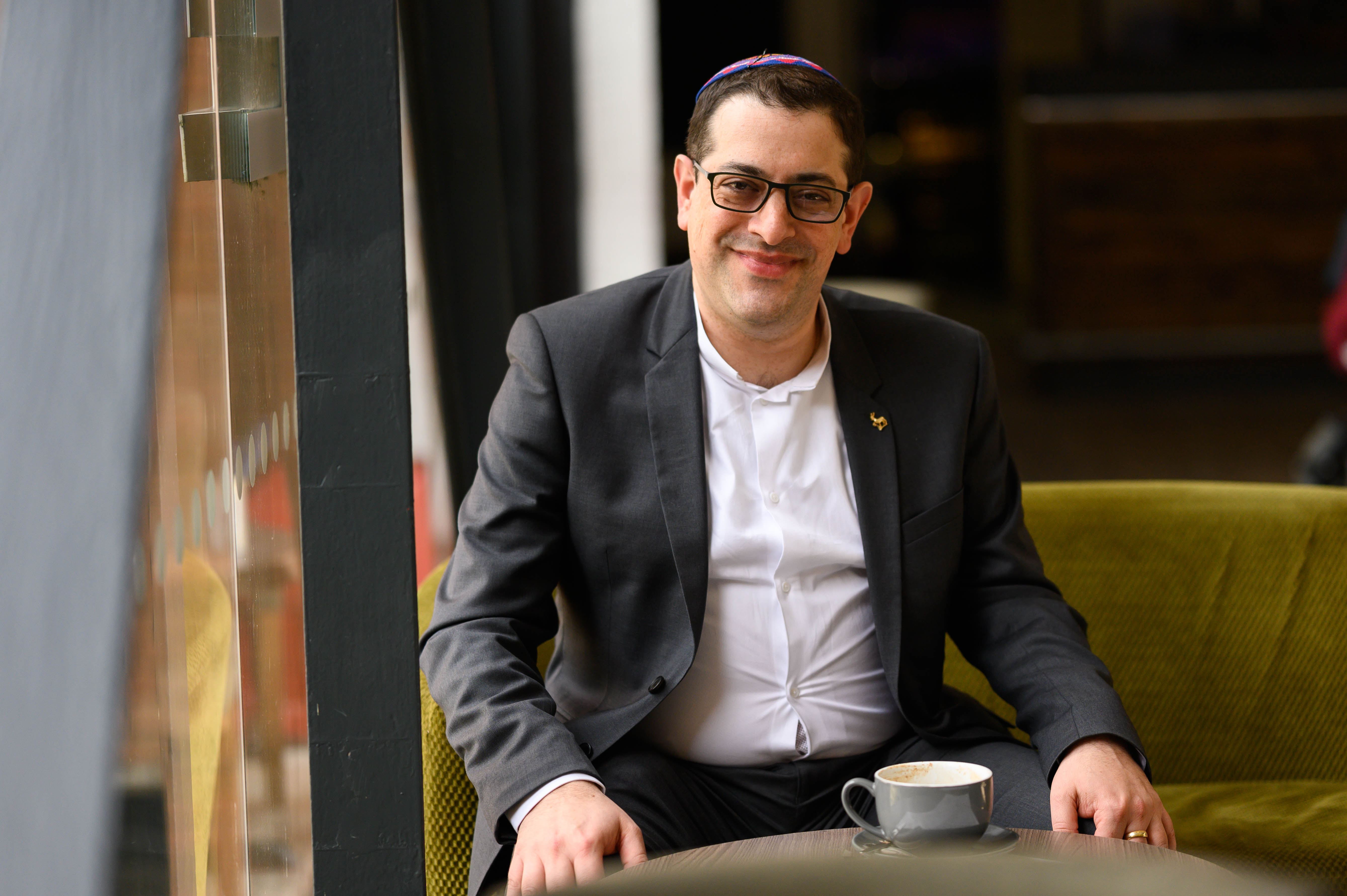 KAICIID Fellow Alex Goldberg smiles at camera as he sits with a cup of coffee