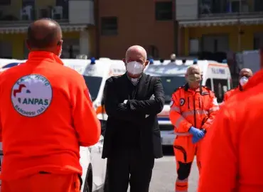 A priest stands next to emergency frontline health workers 