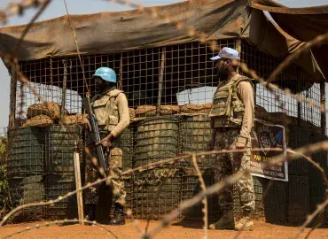 Two UN Peacekeepers stand behind barbed wire 