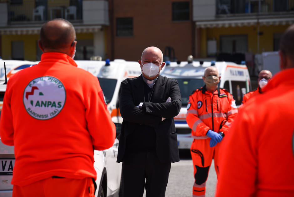 A priest stands next to emergency frontline health workers 