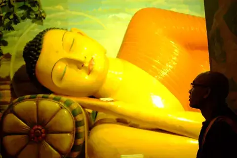 The Venerable Acinna, a member of KIFP 2016, looks on while the tour passes the Reclining Buddha. Painted on the walls of the temple are images from Buddhist scripture that serve as educational material for young Buddhists. Acinna Looks on the Reclining Buddha