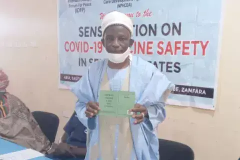 A man holds up his COVID-19 vaccination record. His face, framed by a medical mask and a traditional turban, also bears a certain look of pride in the green piece of paper he holds in his hands. Photo: IDFP