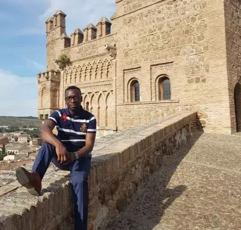 KAICIID Fellow Johnson Amamnsunu sits on a wall in Spain 